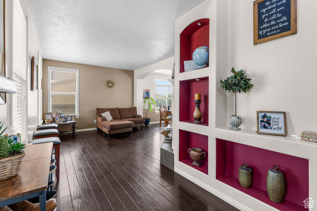 Living area with arched walkways, dark wood-type flooring, and a textured ceiling