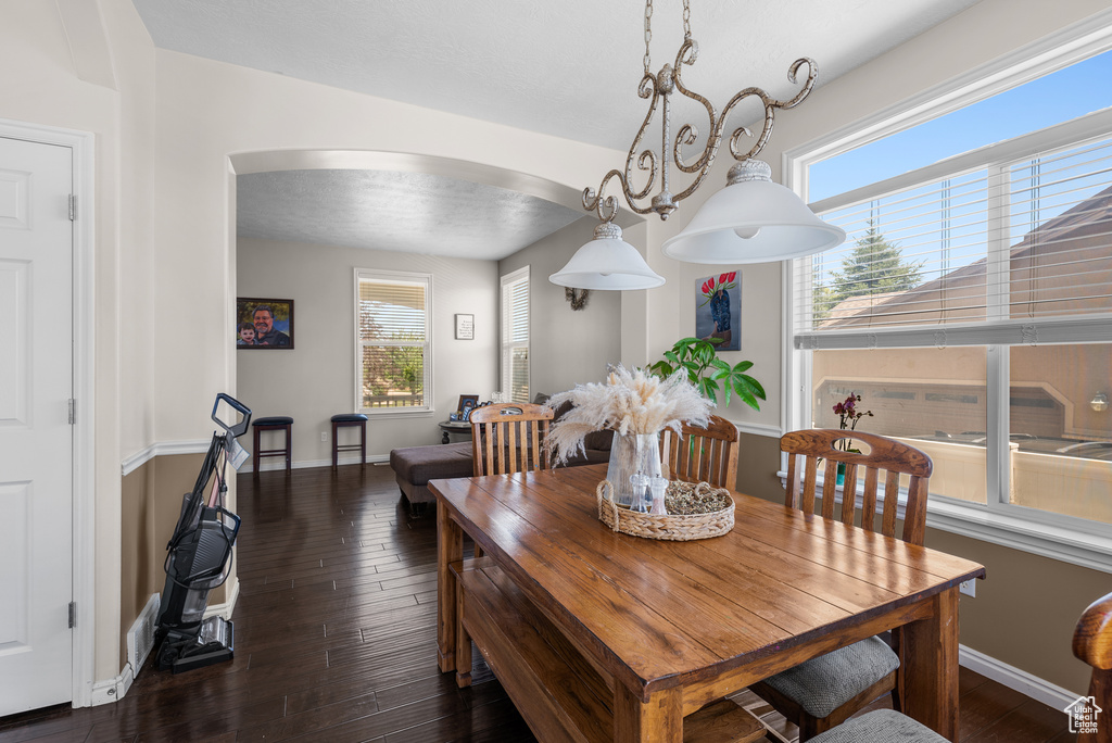 Dining space with arched walkways, plenty of natural light, and wood finished floors