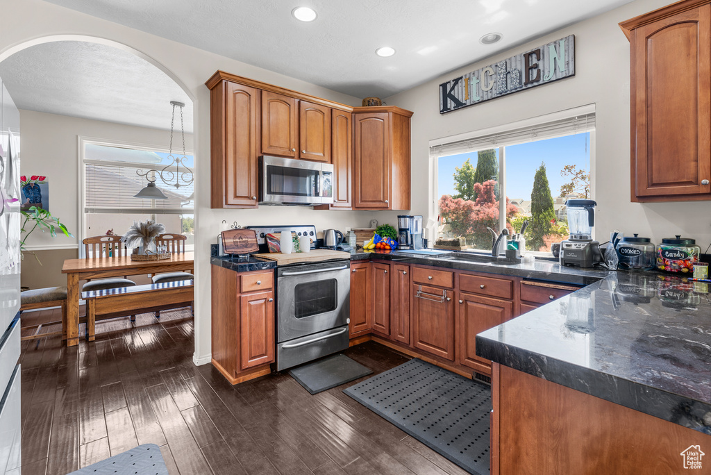 Kitchen with stainless steel appliances, recessed lighting, brown cabinetry, arched walkways, and dark wood finished floors