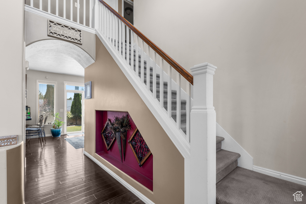 Staircase with arched walkways, wood finished floors, and a high ceiling