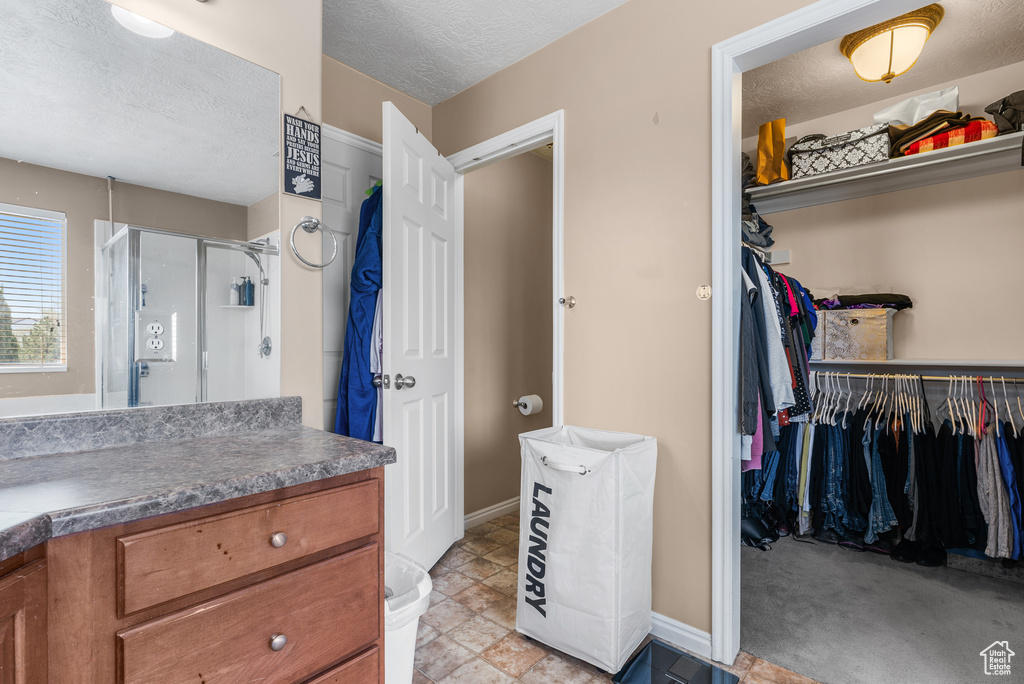 Bathroom with vanity, a stall shower, a walk in closet, and a textured ceiling