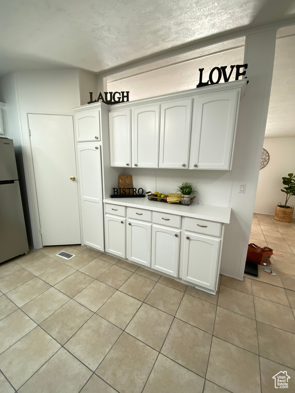 Kitchen featuring freestanding refrigerator, light tile patterned flooring, light countertops, and white cabinetry