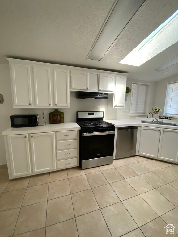 Kitchen featuring stainless steel appliances, under cabinet range hood, light tile patterned floors, light countertops, and white cabinetry