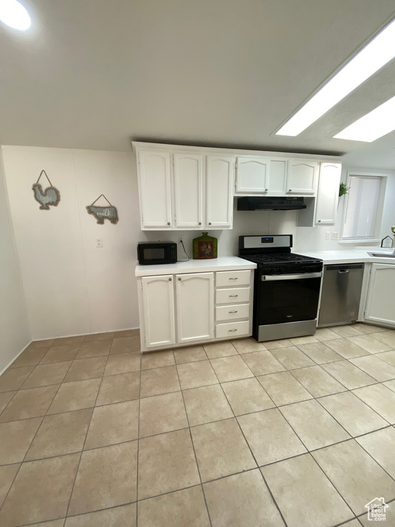 Kitchen with stainless steel appliances, ventilation hood, light tile patterned flooring, and light countertops
