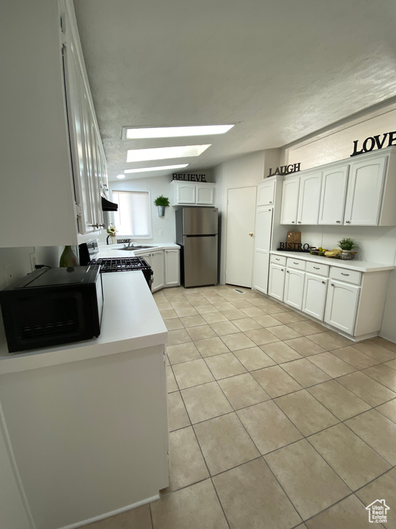 Kitchen featuring freestanding refrigerator, range with gas stovetop, black microwave, light tile patterned floors, and a skylight