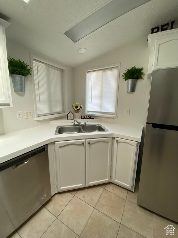 Kitchen featuring appliances with stainless steel finishes, vaulted ceiling, light tile patterned floors, and white cabinetry