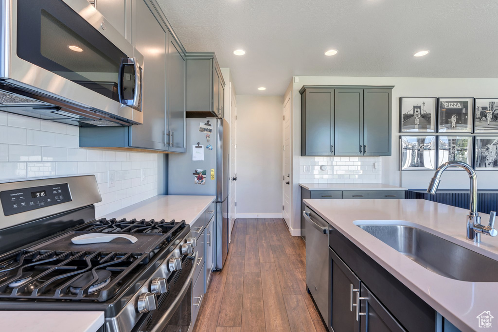 Kitchen with stainless steel appliances, a sink, light countertops, dark wood-style flooring, and baseboards