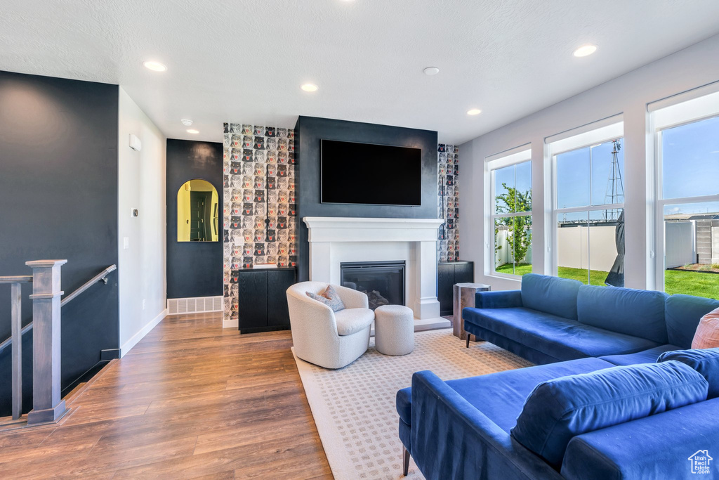 Living room with wood finished floors, a glass covered fireplace, recessed lighting, and baseboards
