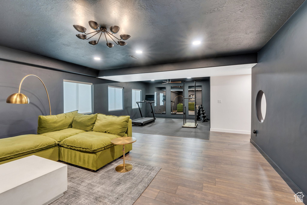 Living room featuring wood finished floors, a textured ceiling, baseboards, a chandelier, and recessed lighting