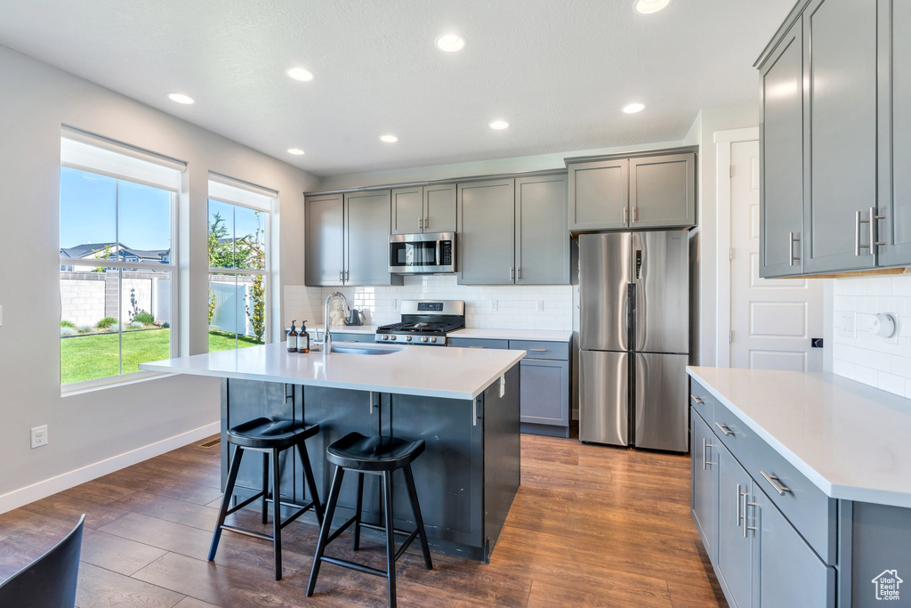 Kitchen with appliances with stainless steel finishes, a sink, gray cabinets, tasteful backsplash, and a kitchen breakfast bar
