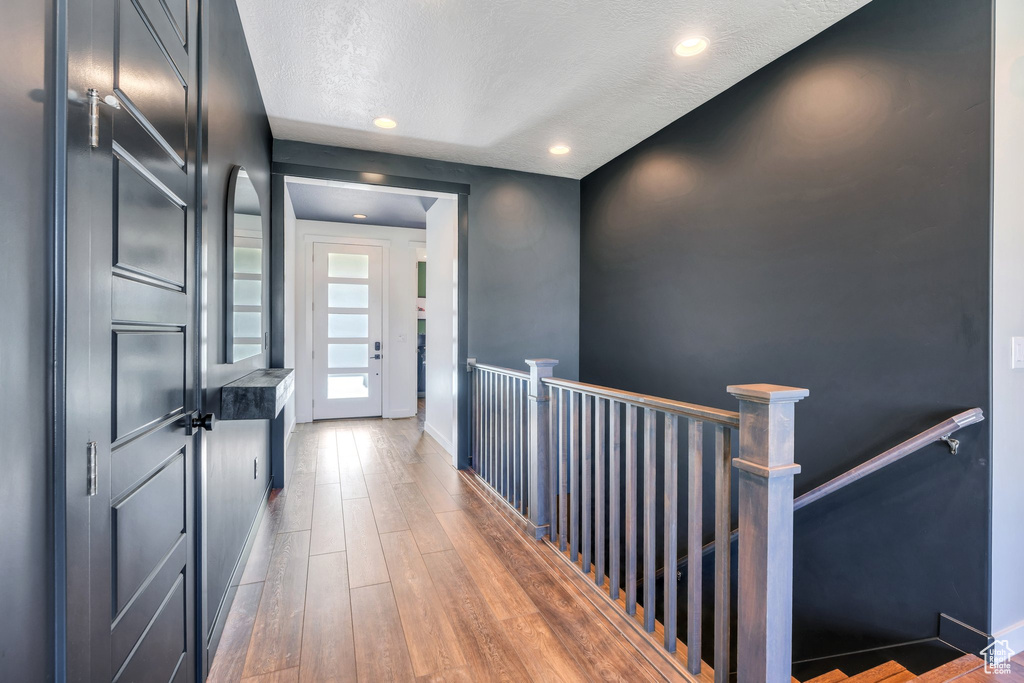 Hall featuring an upstairs landing, wood finished floors, baseboards, recessed lighting, and a textured ceiling