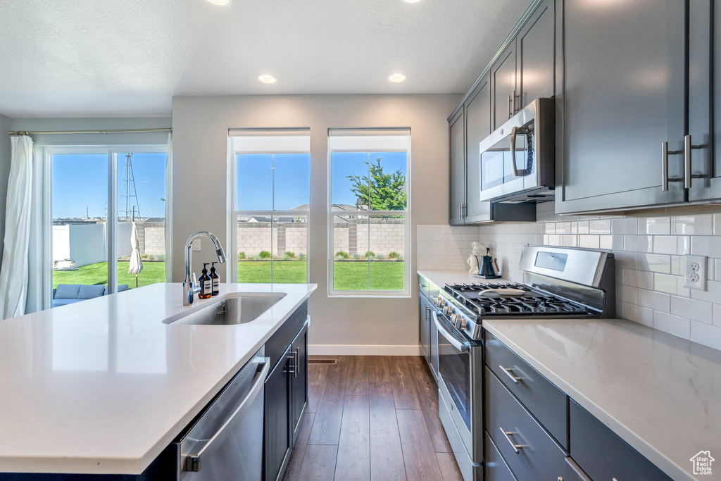 Kitchen featuring stainless steel appliances, a sink, light countertops, dark wood-style floors, and baseboards