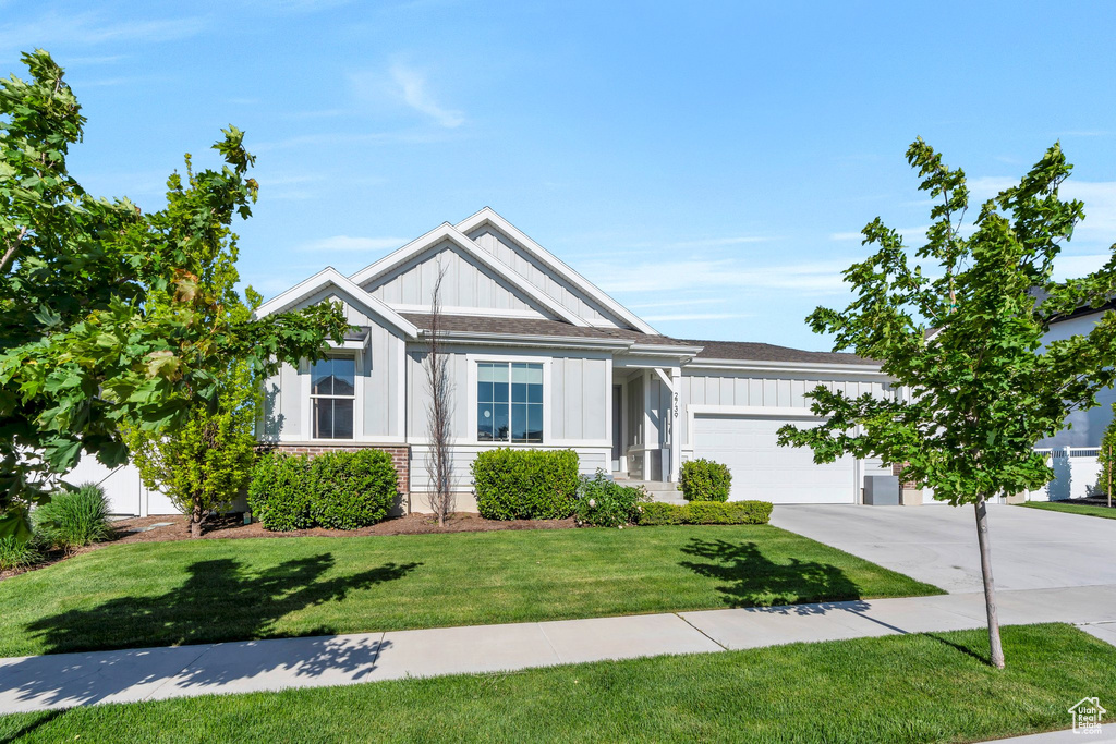 View of front of house with board and batten siding, concrete driveway, a garage, a front lawn, and stone siding