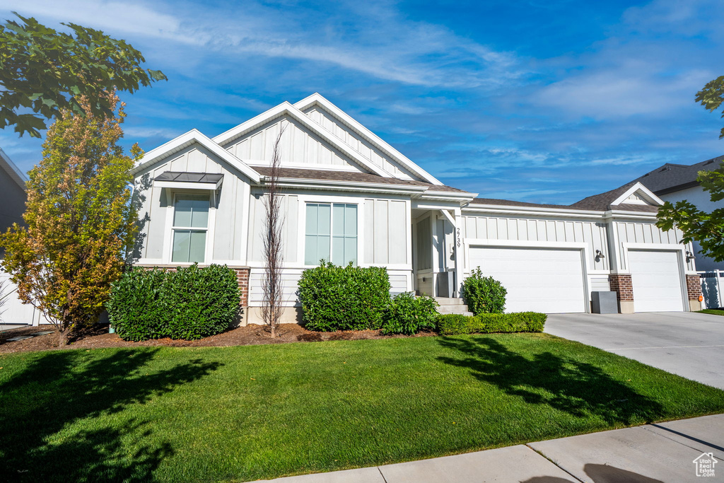 View of front of house featuring board and batten siding, an attached garage, a front yard, and driveway
