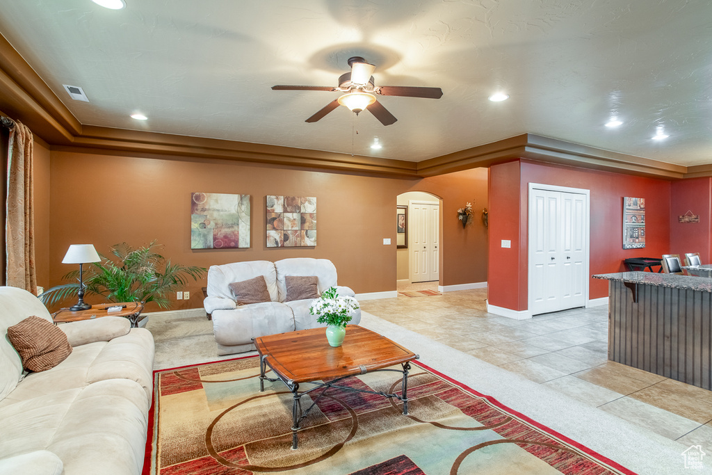 Living room with a tray ceiling, arched walkways, ceiling fan, recessed lighting, and light tile patterned floors
