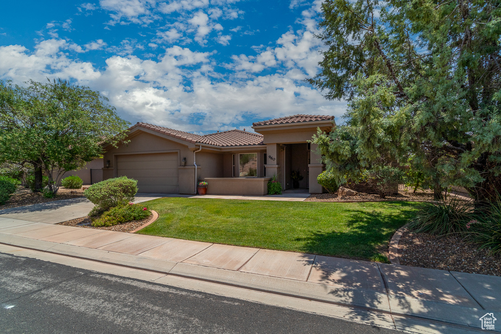 Mediterranean / spanish home with a tile roof, stucco siding, a garage, a front lawn, and concrete driveway