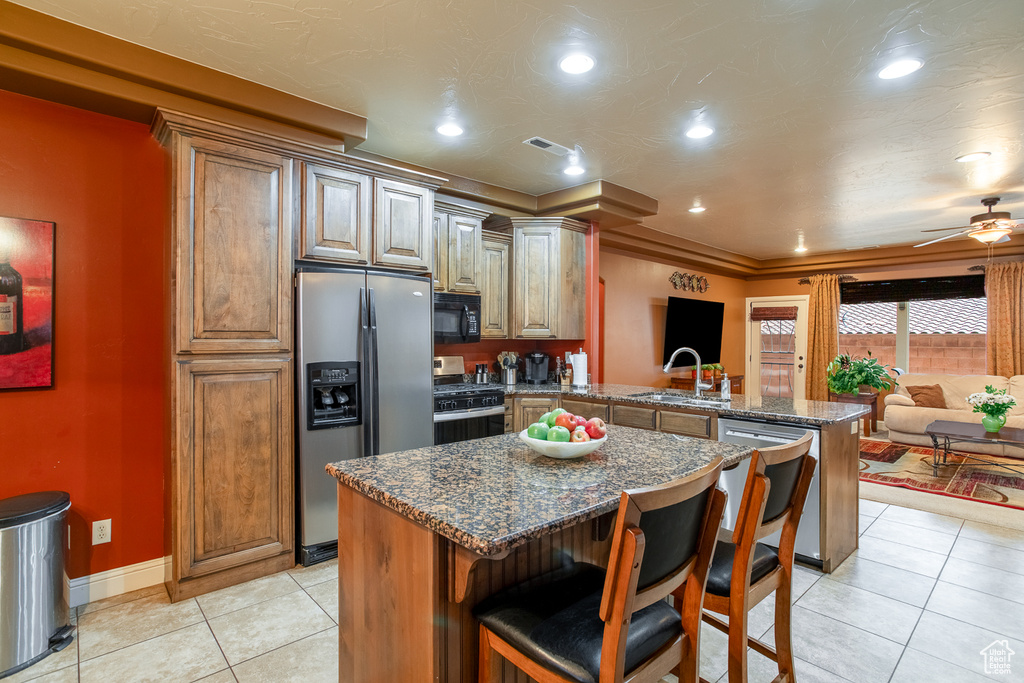 Kitchen featuring stainless steel appliances, a peninsula, light tile patterned floors, ceiling fan, and a breakfast bar area