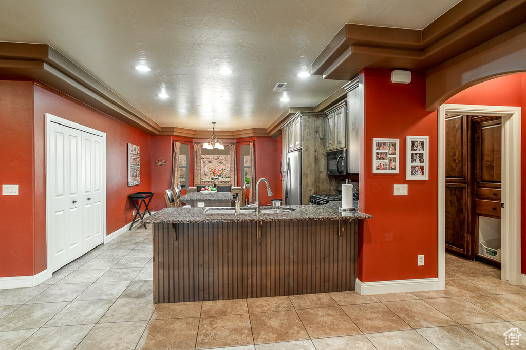Kitchen featuring black microwave, freestanding refrigerator, a peninsula, dark stone countertops, and light tile patterned floors