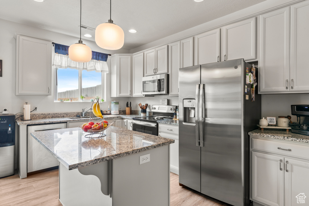 Kitchen with appliances with stainless steel finishes, recessed lighting, light stone countertops, a center island, and light wood-style floors