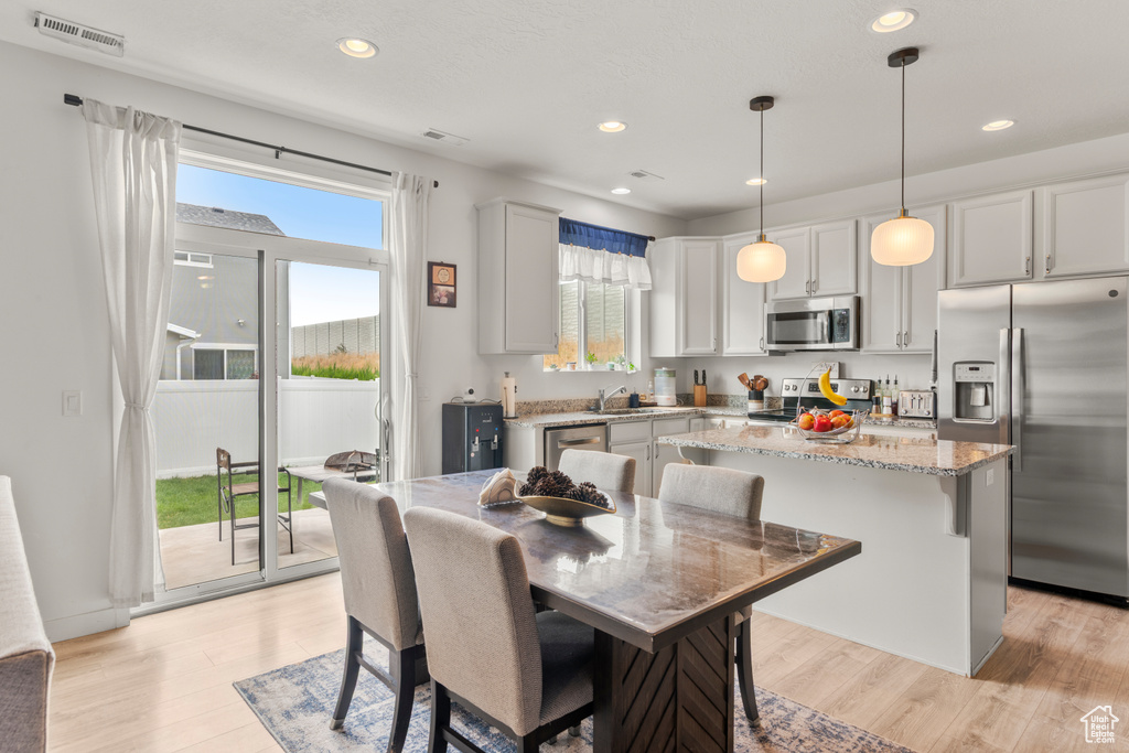 Kitchen with stainless steel appliances, a kitchen island, light wood-style flooring, light stone counters, and pendant lighting