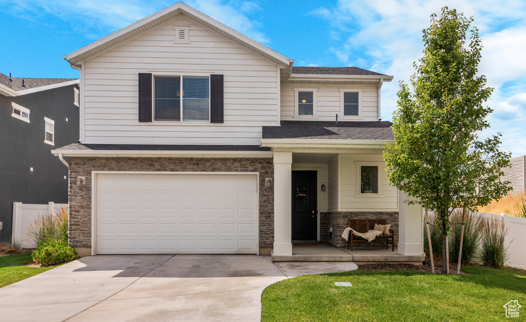View of front of property with stone siding, driveway, an attached garage, and a shingled roof