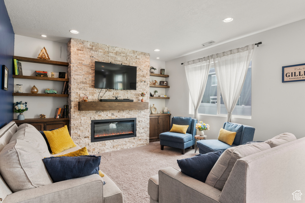 Living room featuring a stone fireplace, carpet flooring, recessed lighting, and built in features