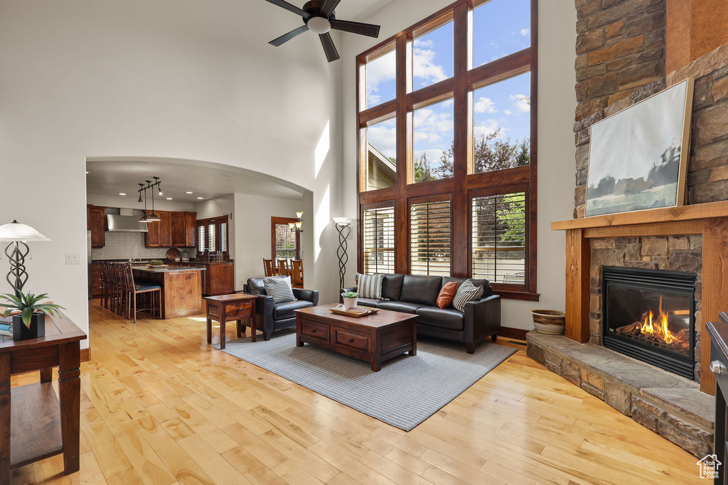 Living area with a towering ceiling, a ceiling fan, arched walkways, light wood-type flooring, and a fireplace