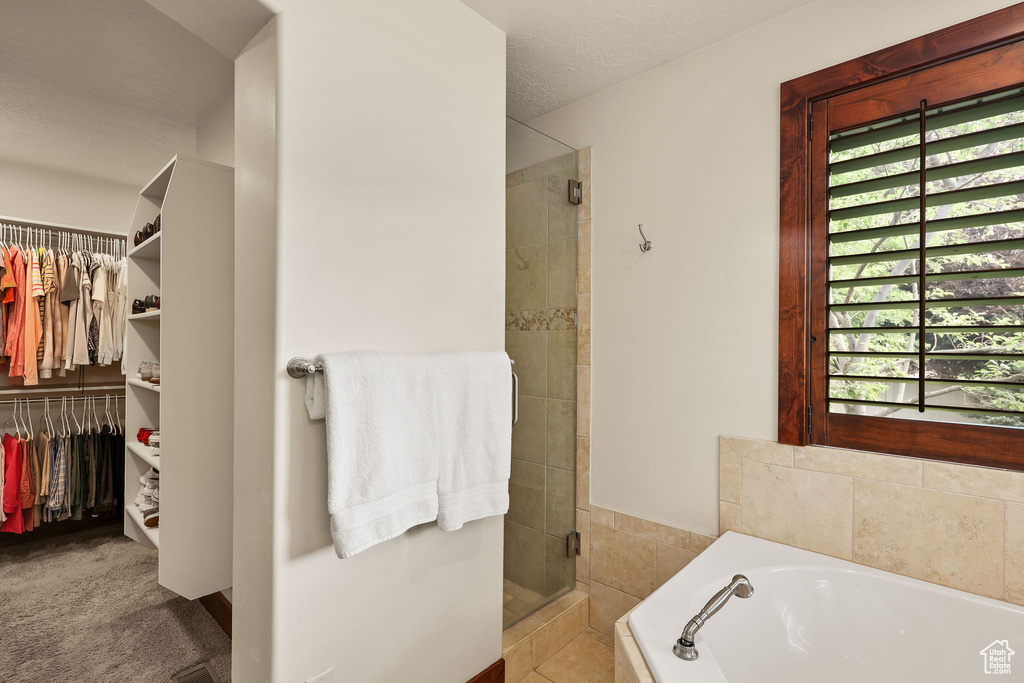Bathroom featuring a shower stall, a garden tub, a walk in closet, and a textured ceiling