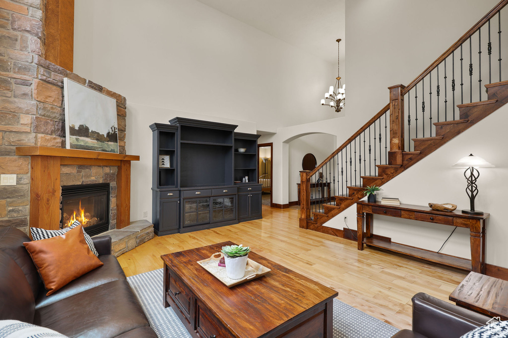 Living area featuring a towering ceiling, light wood-style flooring, a stone fireplace, stairway, and a chandelier