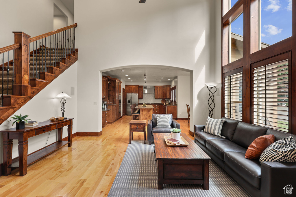 Living room with a high ceiling, light wood-type flooring, arched walkways, stairway, and recessed lighting