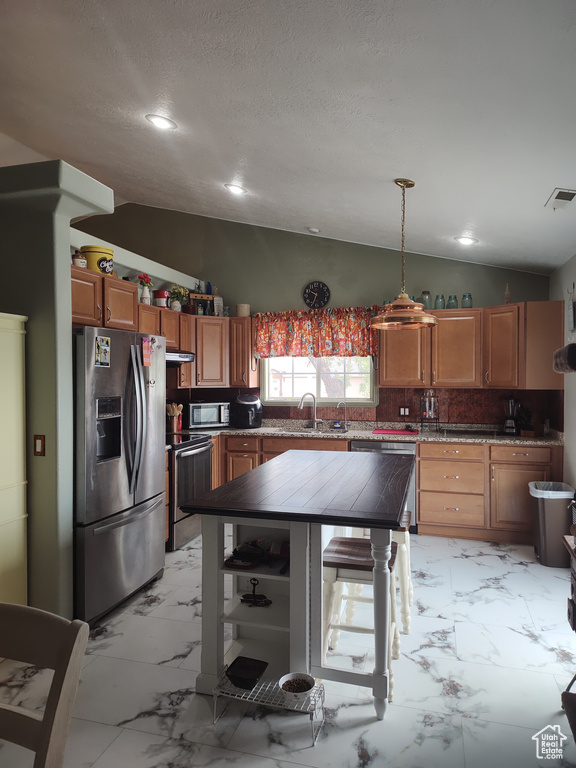 Kitchen featuring appliances with stainless steel finishes, vaulted ceiling, light marble finish floors, backsplash, and brown cabinetry