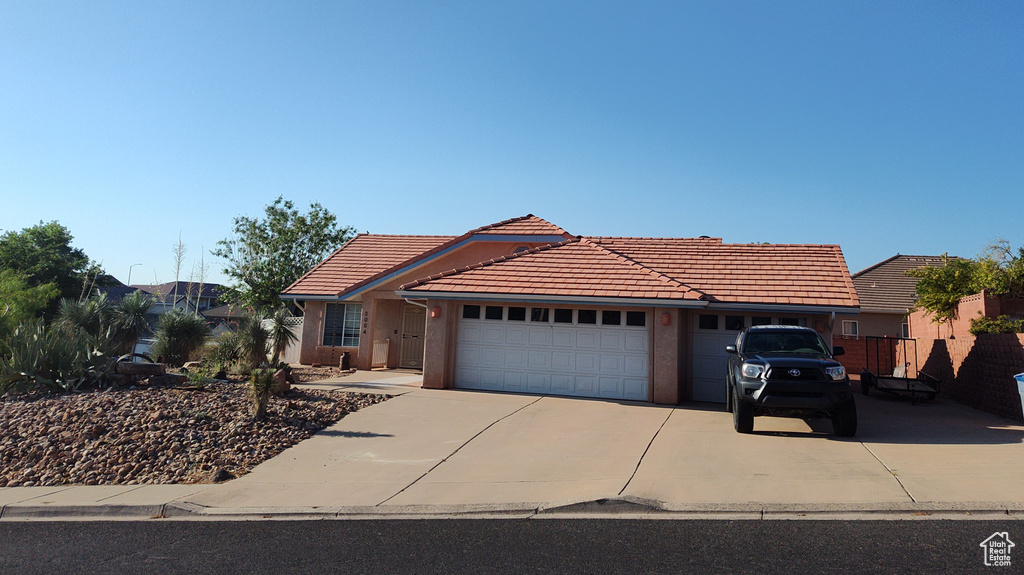 View of front facade featuring a tile roof, driveway, an attached garage, and stucco siding