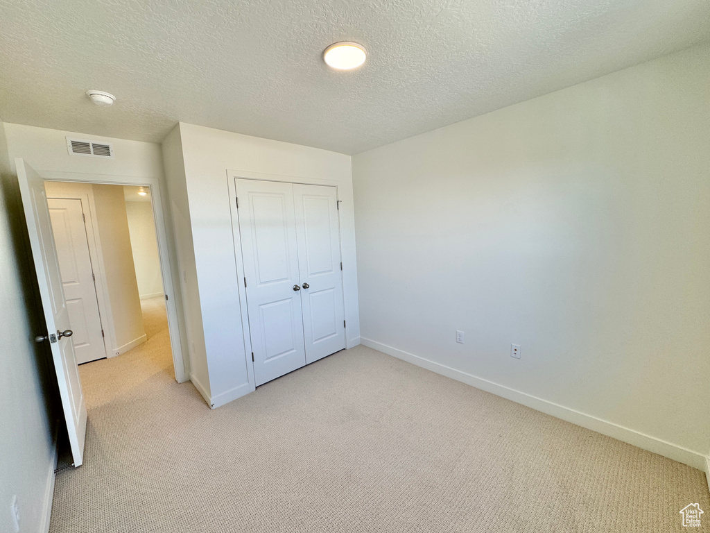 Unfurnished bedroom featuring light carpet, a closet, and a textured ceiling