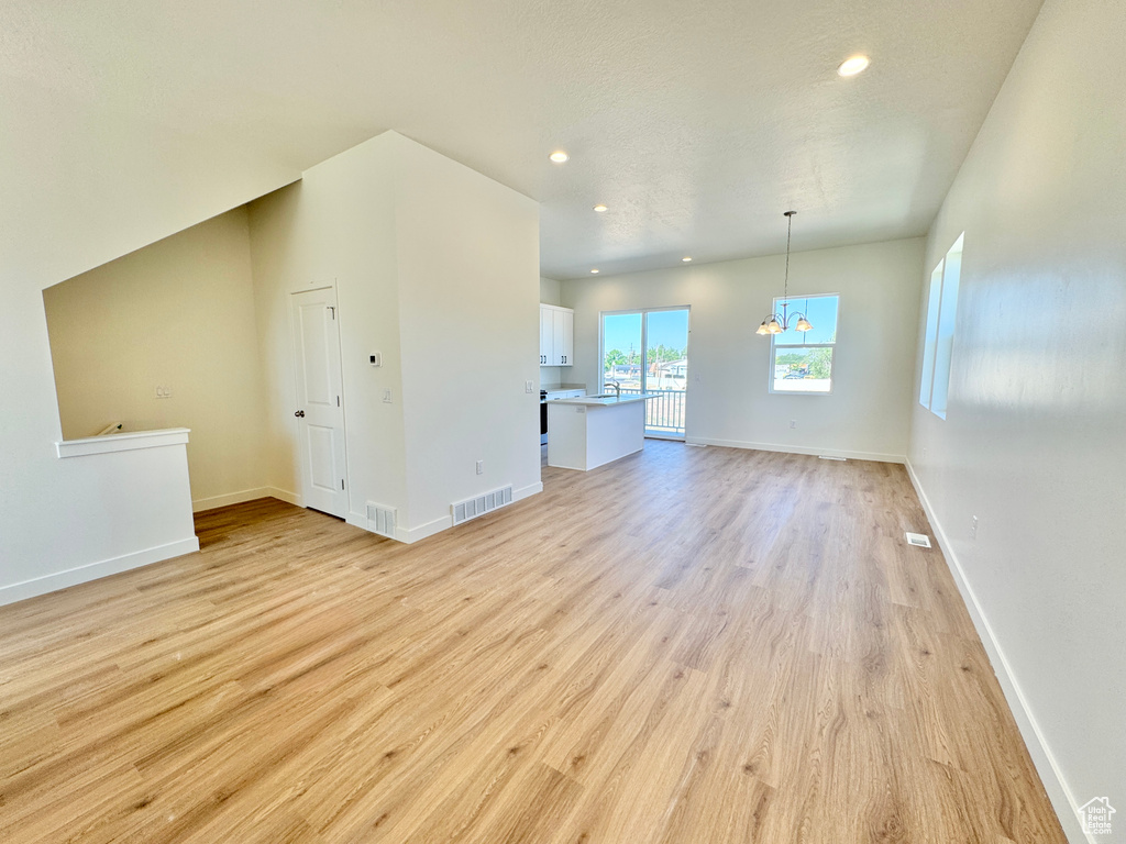 Unfurnished living room with light wood-type flooring, recessed lighting, and a chandelier