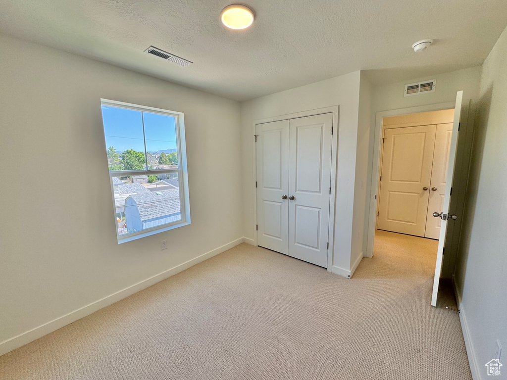 Unfurnished bedroom featuring light colored carpet, a textured ceiling, and a closet