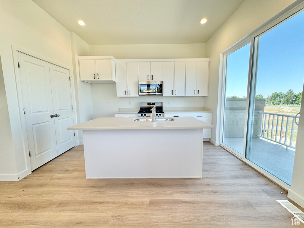 Kitchen featuring stainless steel appliances, white cabinetry, light countertops, light wood-style floors, and recessed lighting