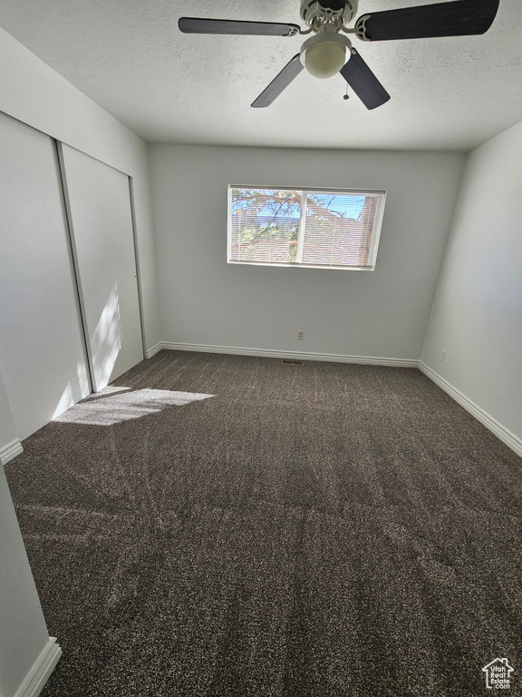 Unfurnished bedroom featuring a closet, a textured ceiling, dark colored carpet, and a ceiling fan