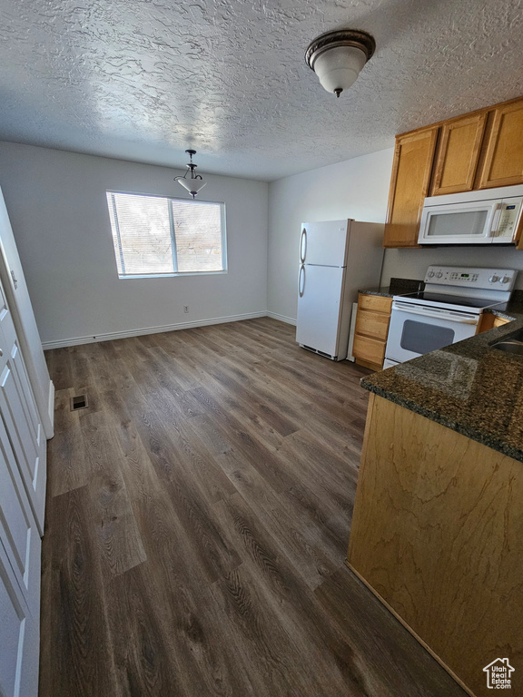 Kitchen featuring white appliances, dark wood-style flooring, a textured ceiling, brown cabinetry, and dark stone countertops