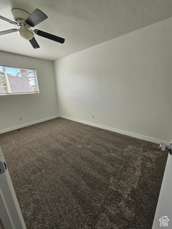 Unfurnished room with dark colored carpet, ceiling fan, and a textured ceiling