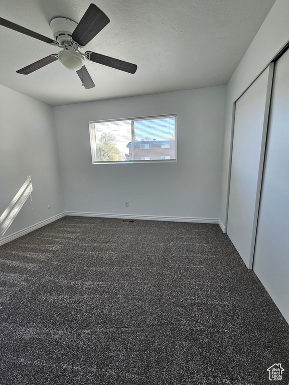 Unfurnished bedroom with dark colored carpet, a ceiling fan, and a closet