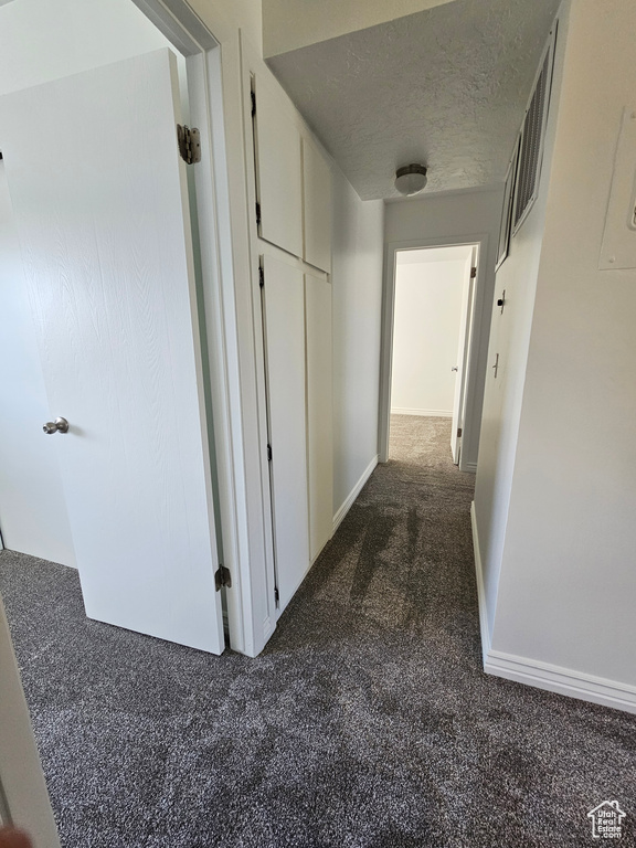 Hall featuring dark colored carpet and a textured ceiling
