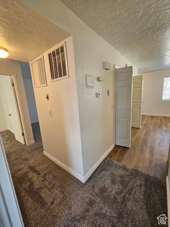 Hall featuring a textured ceiling, carpet flooring, and wood finished floors