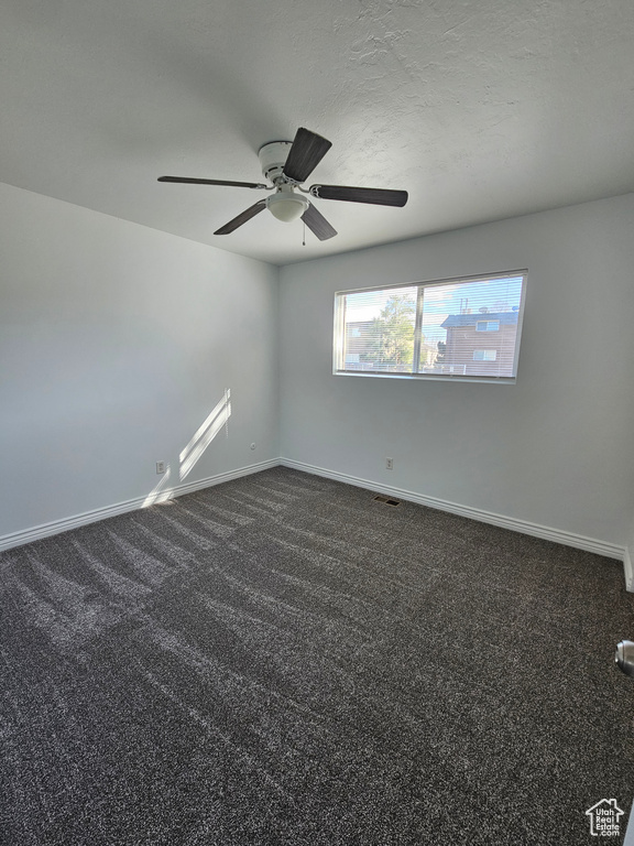Spare room with a ceiling fan and dark colored carpet