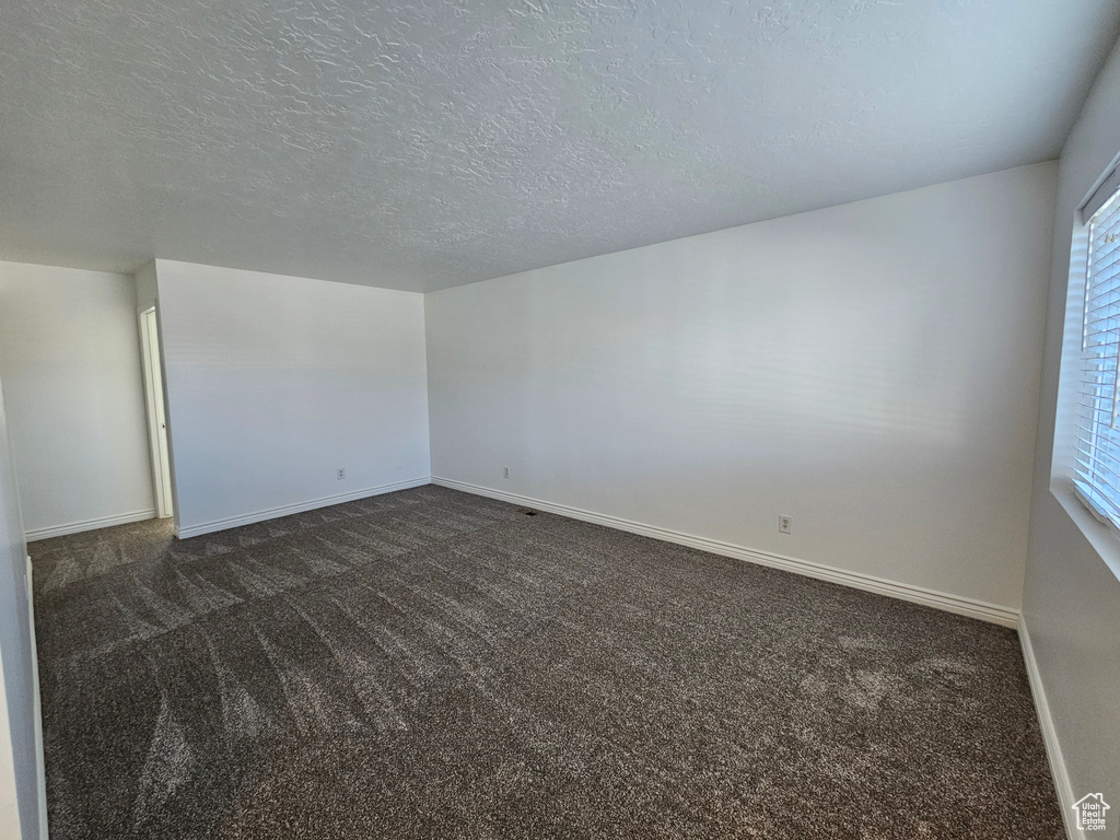 Unfurnished room featuring dark colored carpet and a textured ceiling