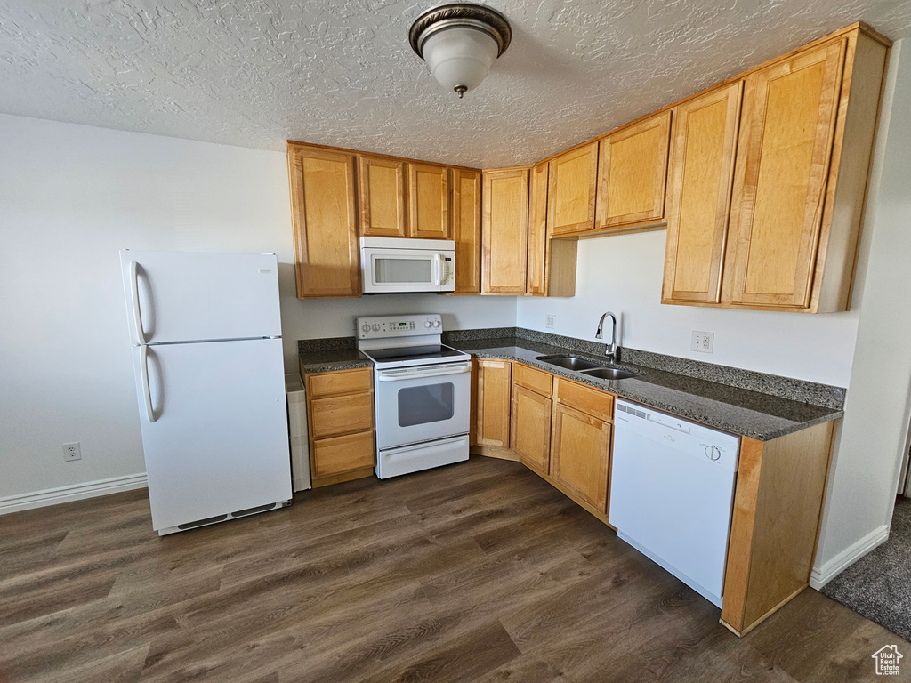 Kitchen with white appliances, dark countertops, dark wood-type flooring, and a textured ceiling