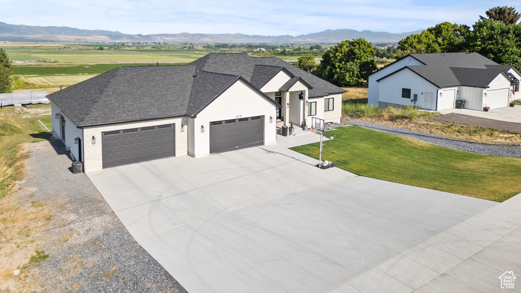 View of front of property with a garage, driveway, a front lawn, a mountain view, and a shingled roof