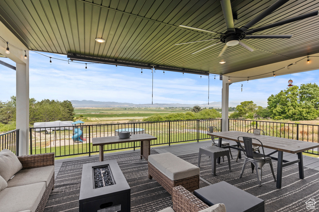 Deck featuring an outdoor living space with a fire pit, a view of rural / pastoral area, a ceiling fan, a mountain view, and outdoor dining area