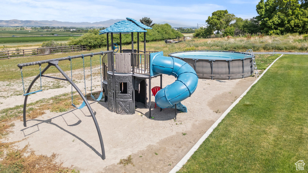 Community playground featuring an outdoor pool, a mountain view, and a rural view
