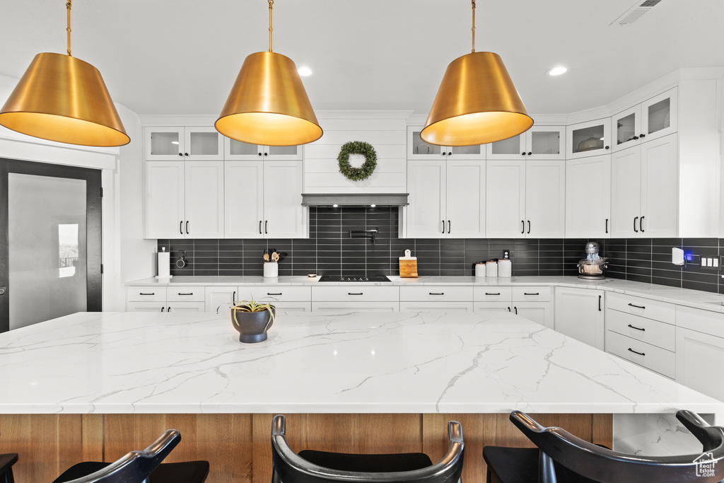 Kitchen with black electric cooktop, backsplash, white cabinetry, and a breakfast bar area