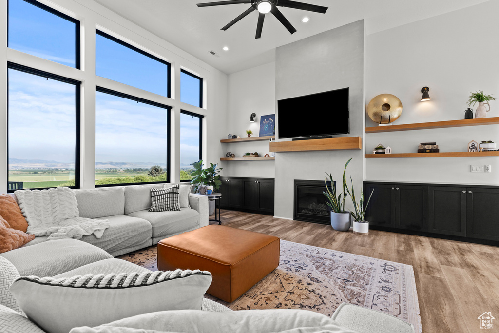 Living area with ceiling fan, light wood-style flooring, recessed lighting, a glass covered fireplace, and a high ceiling
